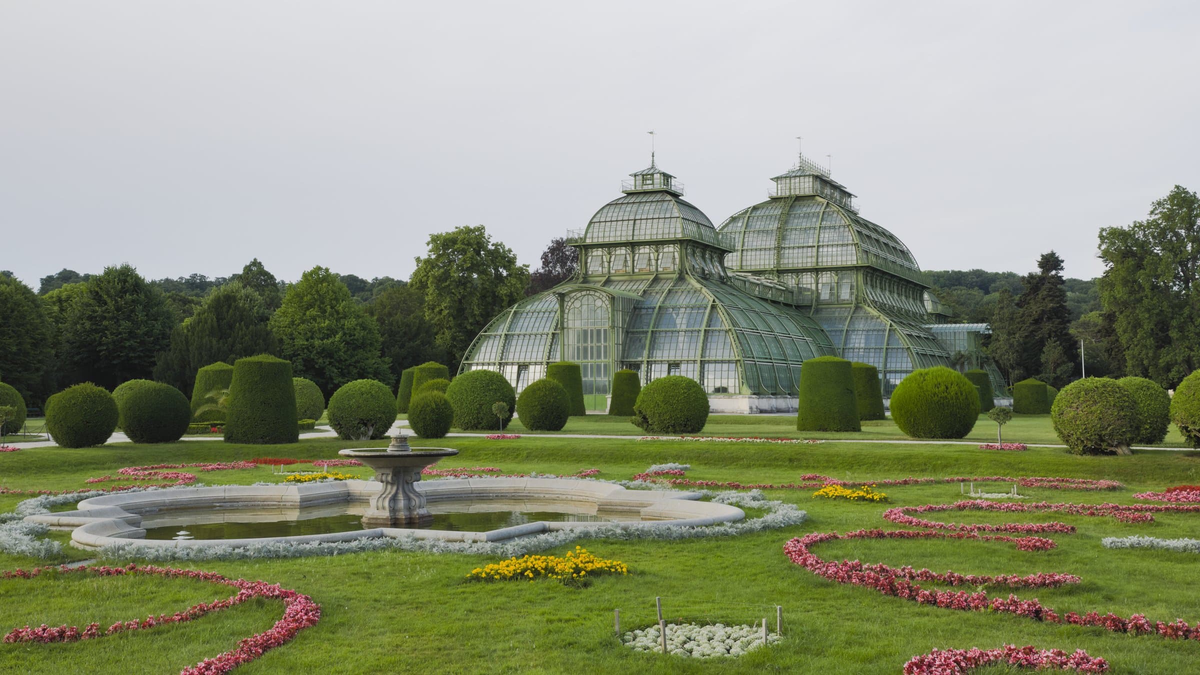 Palmenhaus Schönbrunn hinter Rasenflächen und farbigen Blumenbeeten