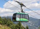 Grüne Kabine der Raxseilbahn über dem Wald mit Bergpanorama im Hintergrund