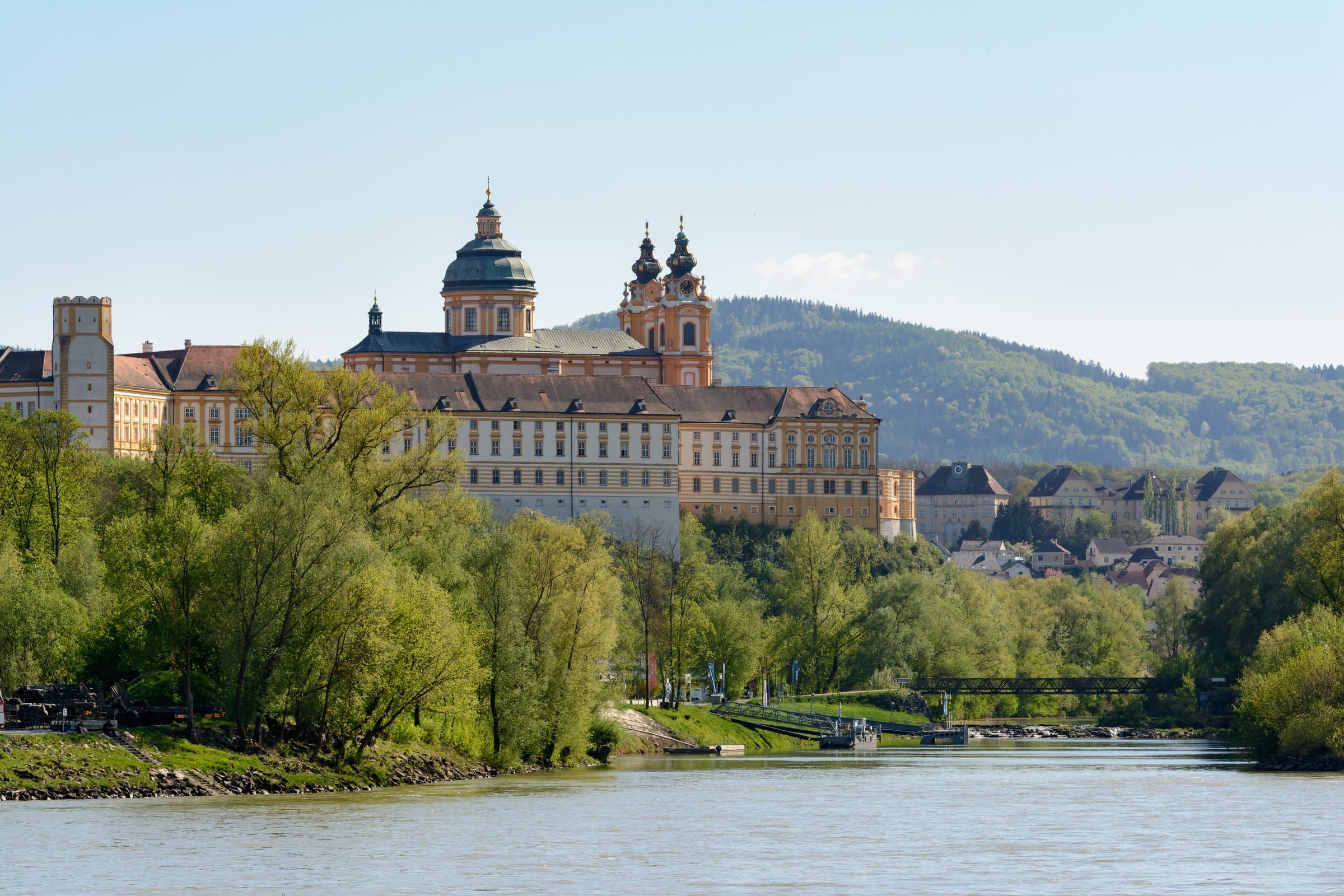 Stift Melk mit gelber Fassade und zwei Kirchtürmen über dem bewaldeten Donauufer