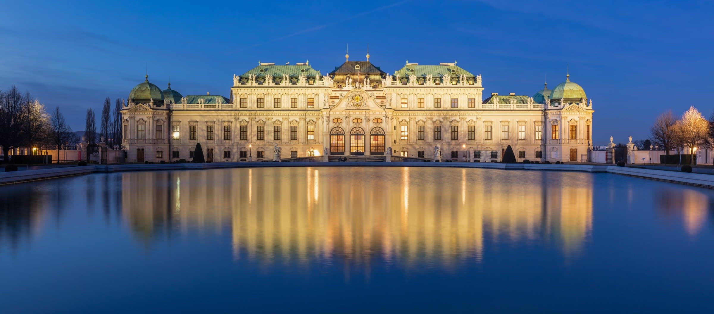 Beleuchtetes Oberes Belvedere und seine Spiegelung im Wasserbecken bei Nacht