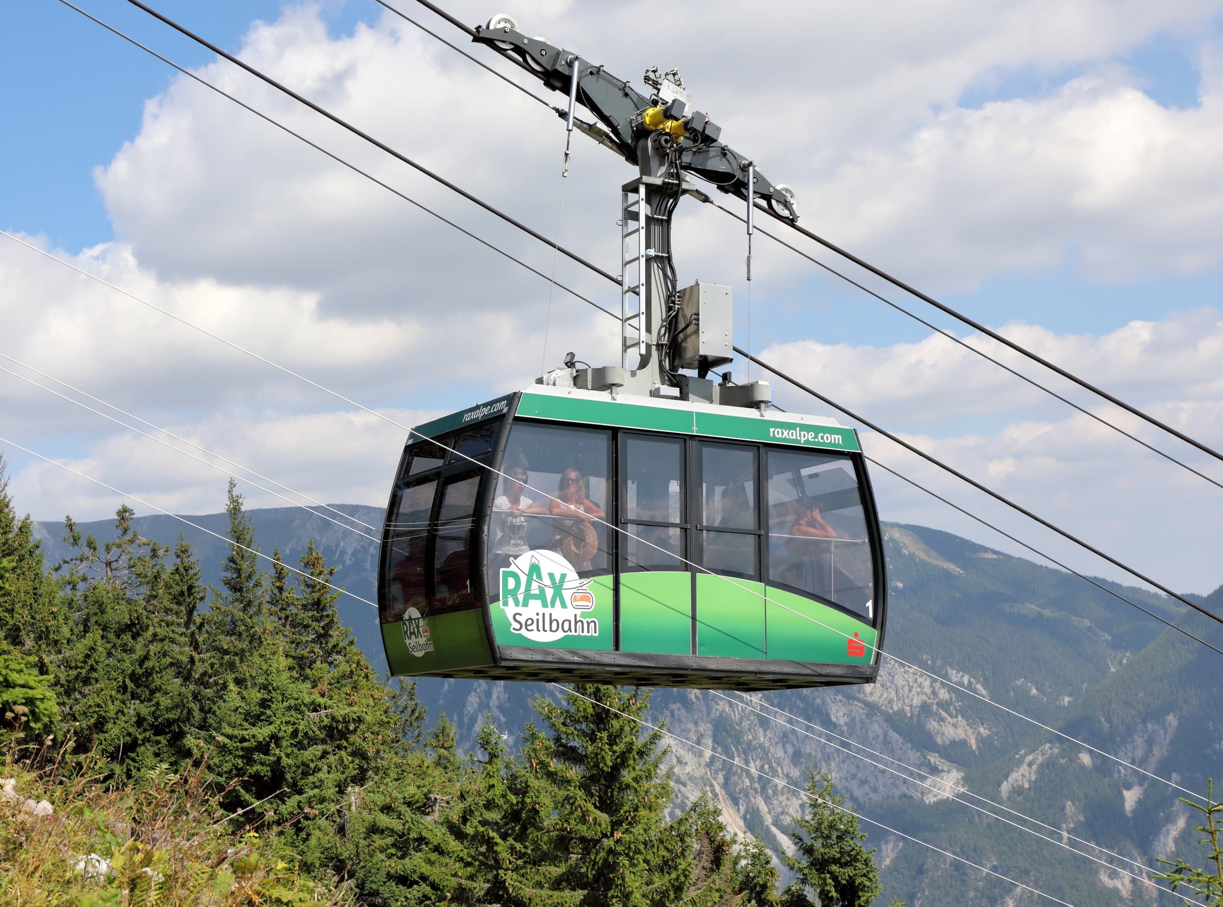 Grüne Kabine der Raxseilbahn über dem Wald mit Bergpanorama im Hintergrund