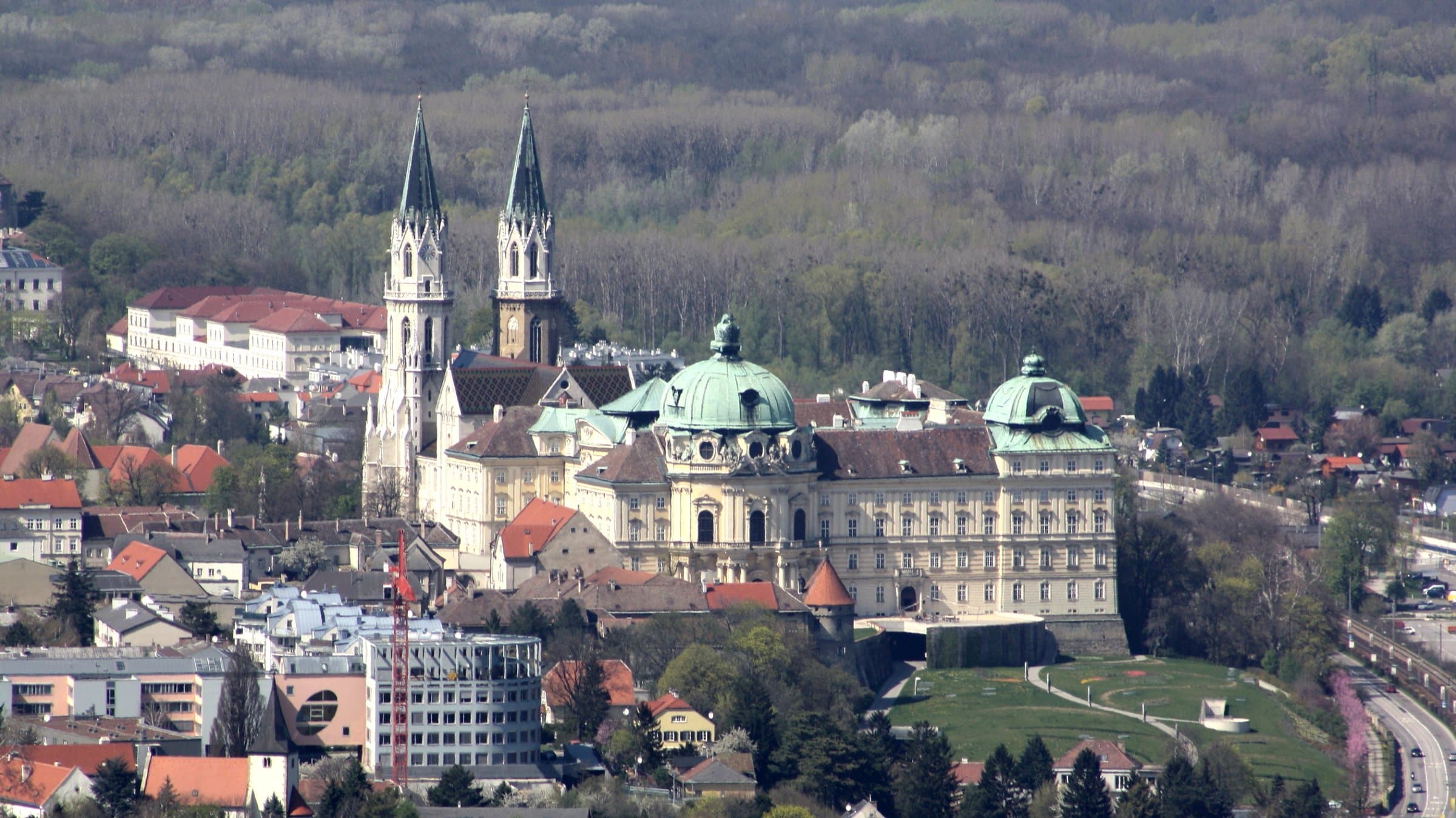 Stift Klosterneuburg mit Kirchtürmen und grünen Kuppeln vor bewaldeten Hügeln