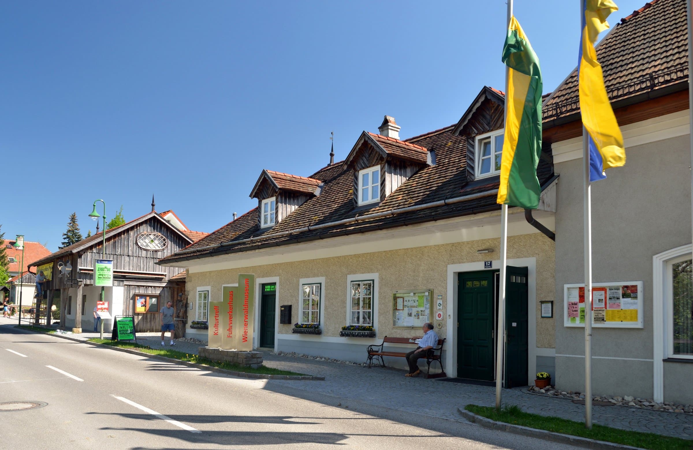 Gelbe Straßenfassade des Wienerwaldmuseums Eichgraben mit Fahnen am Eingang